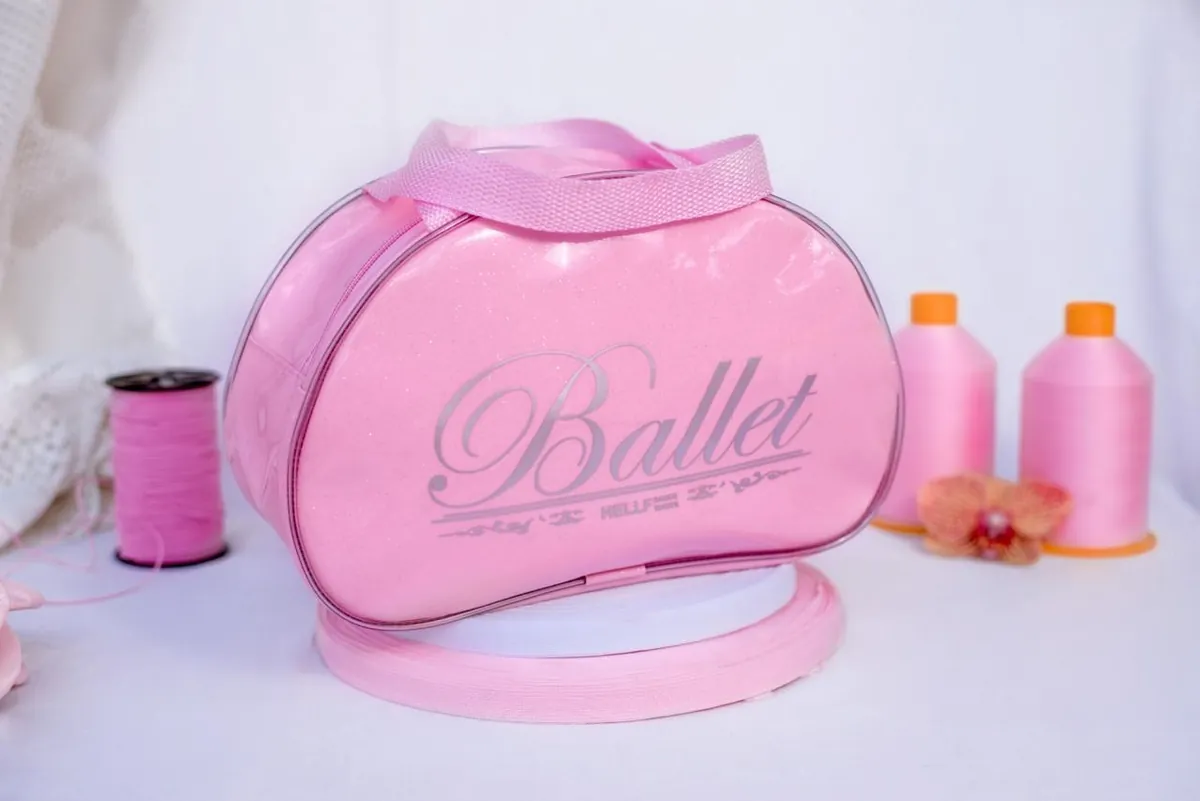 Bag oval rosa com glitter e a estampa Ballet, ao lado de cones de linha rosa usados na produção.