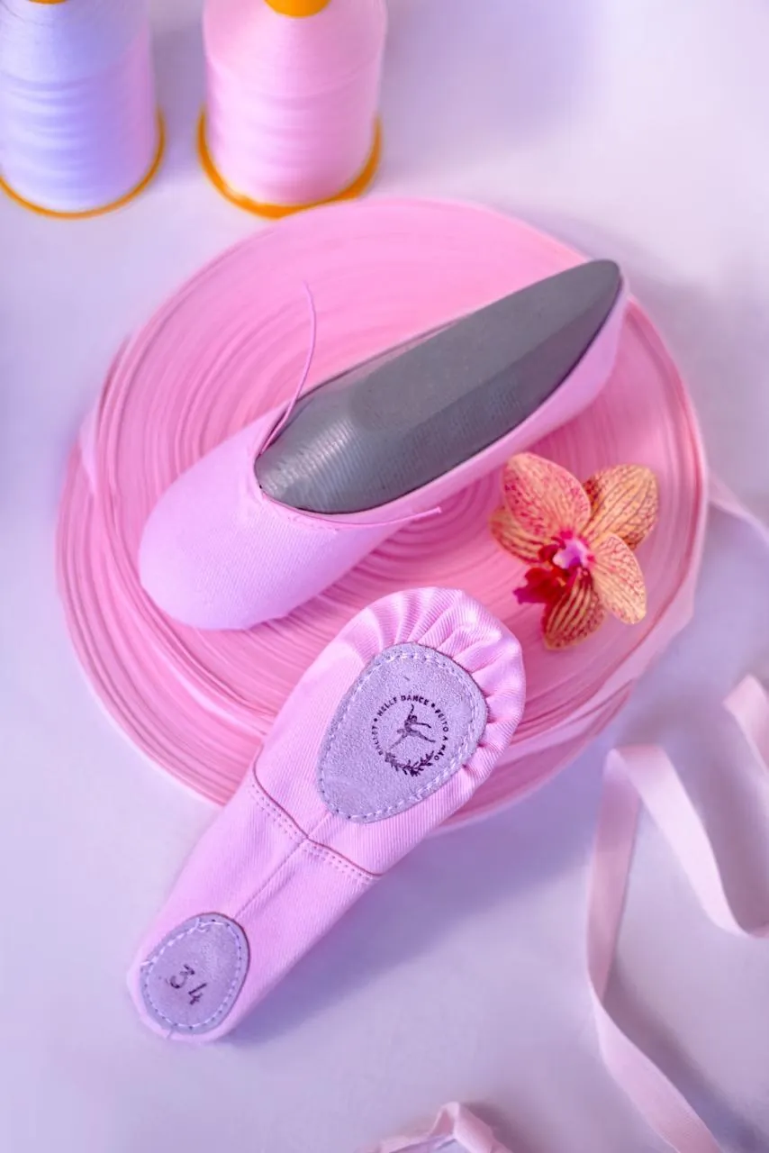 Sapatilhas rosa de sola inteira e sola dividida sobre rolo de fita, com a palmilha de camurça carimbada com a marca e a inscrição feito à mão.