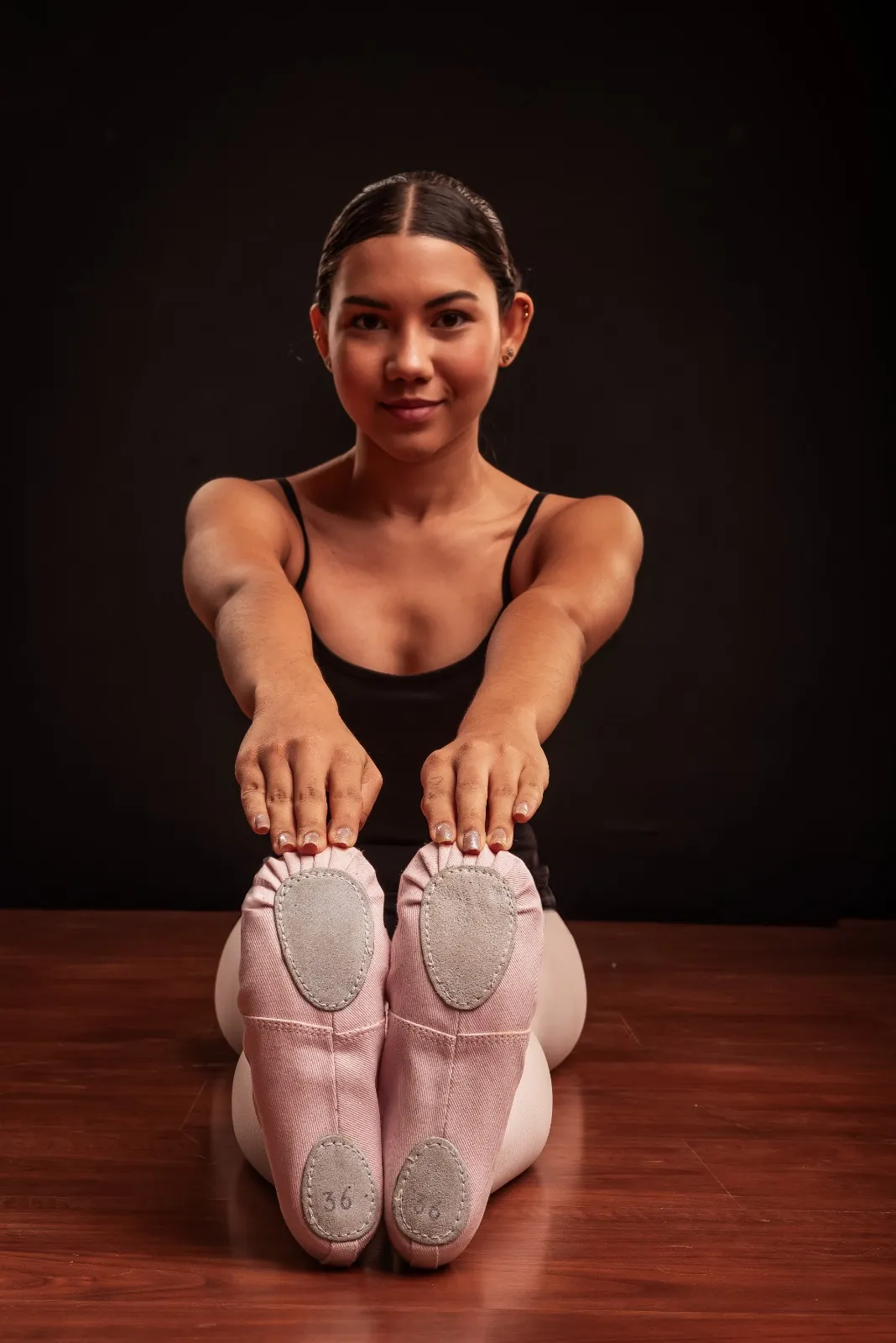 Bailarina sentada mostrando as solas de camurça de suas sapatilhas rosa tamanho 36.