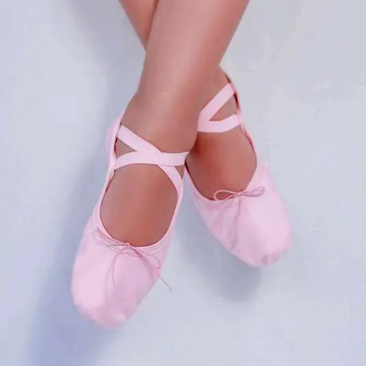 Pés de bailarina calçando sapatilha strech rosa de sola dividida com elástico cruzado.
